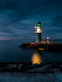A serene lighthouse standing tall against a navy blue night sky, golden rays of light casting warmth over calm ocean waves.