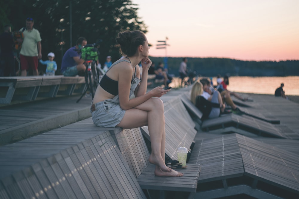 Frau sitzt auf Holzbank in der Nähe von Menschen und Strand