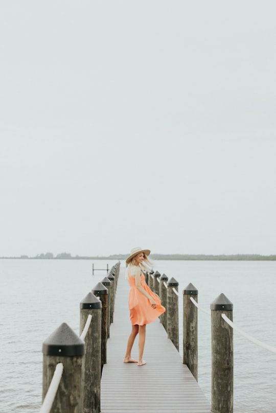 woman in orange spaghetti strap mini dress standing on brown wooden dock during daytime in Port Charlotte United States