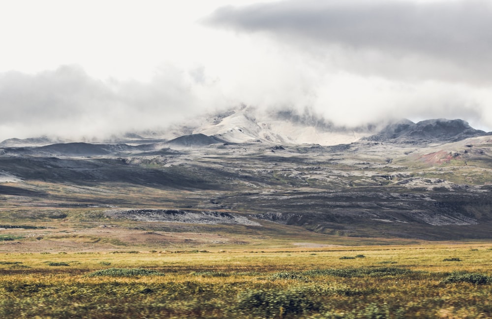 green field surrounded by hill under white clouds