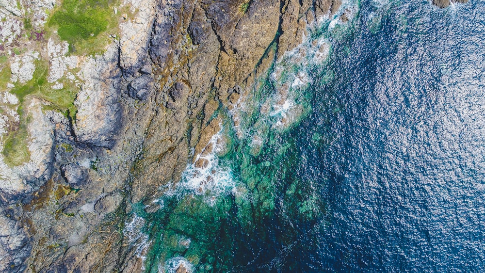 잔디로 덮인 산 근처의 바위 해안의 항공 사진