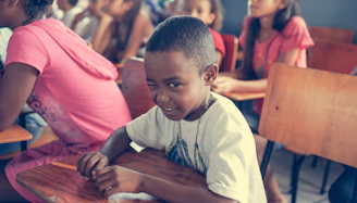 A young boy sitting at a desk, smiling as he interacts with a friendly robot beside him.