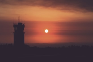 An air traffic control tower silhouetted against a vibrant dawn sky, bustling with activity.