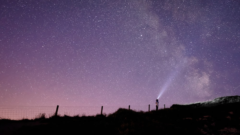 silhouette of person standing on hills under purple and white sky