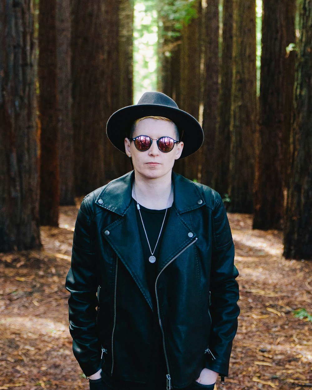 man in black full-zip jacket standing between green trees