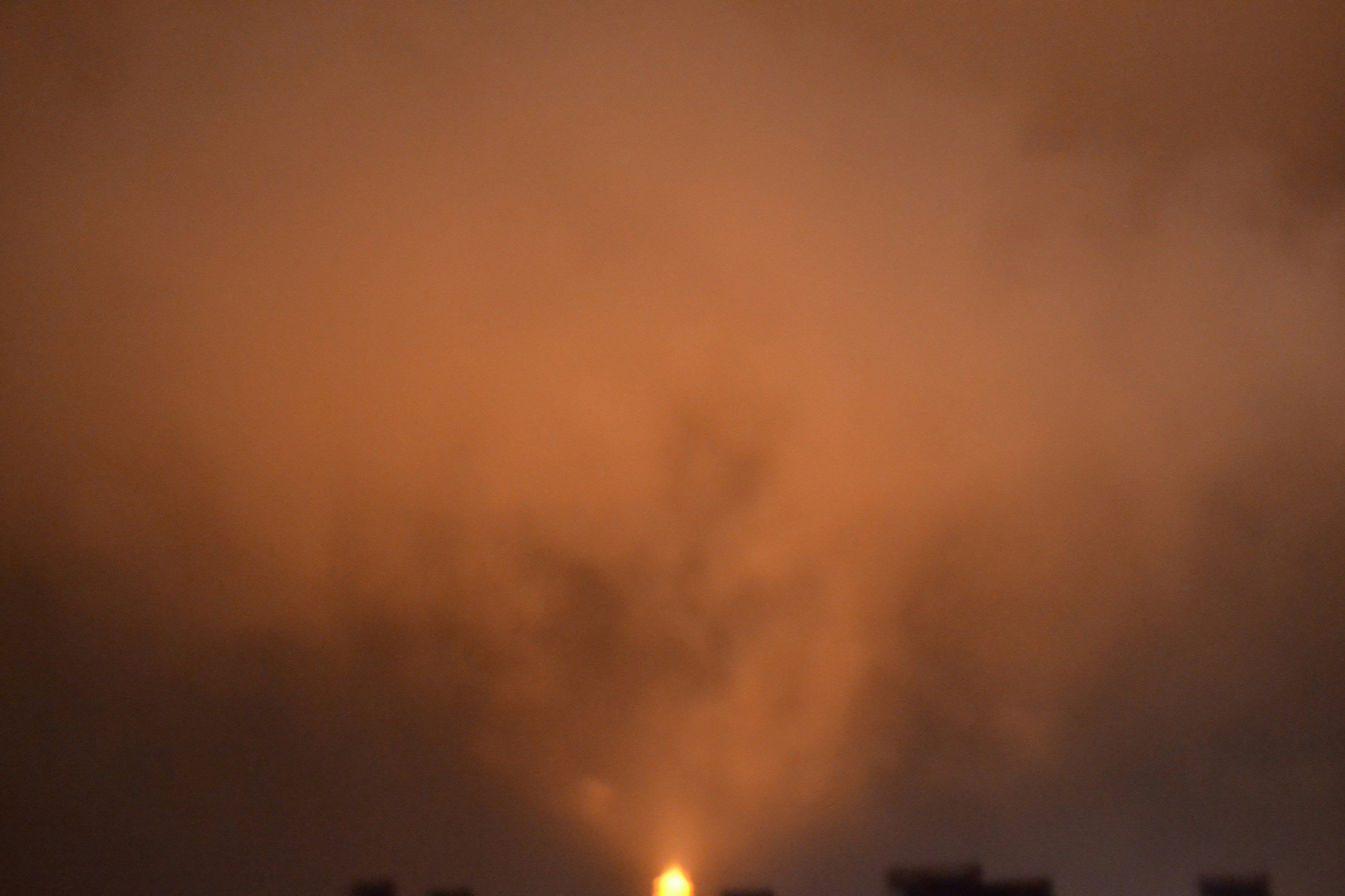 Destroyed urban buildings at night with orange fires burning inside ruined structures, smoke rising, dark sky, war damage in a Middle Eastern city