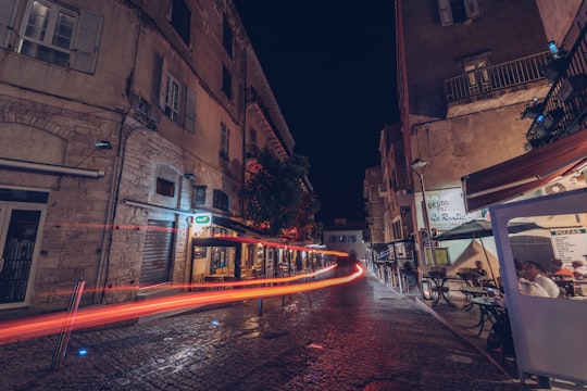 timelapse photograhy of orange light and group of people sitting on patio set beside commercial buildings during nighttime in Bonifacio France