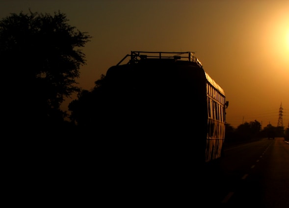 A sleek Raj Express luxury bus parked by a scenic road at sunset.