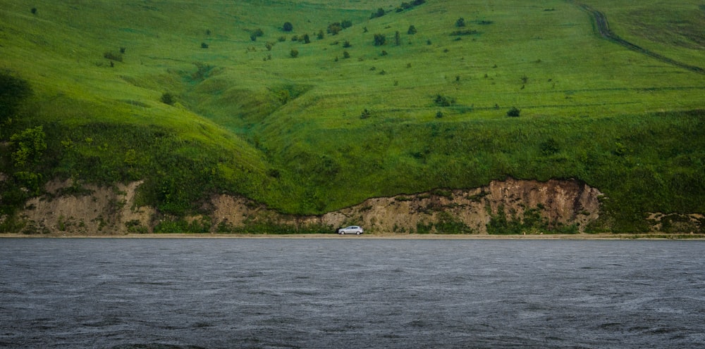 white car travelling on road in middle of hill and sea