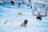 Young female water polo player celebrating a goal with teammates in a sunlit pool.
