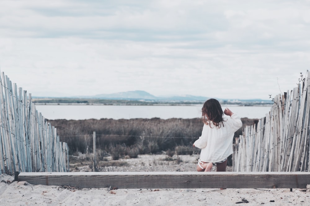 girl stepping down on wooden steps with wooden fence towards brown grassfield