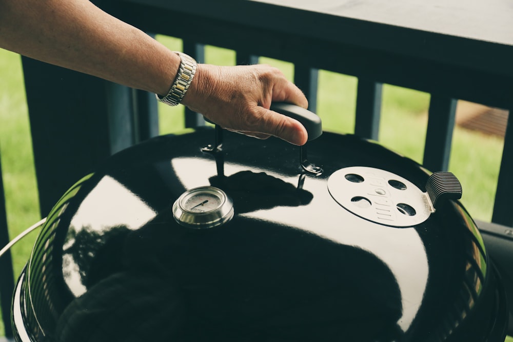 person holding kettle grill's cover near balustrade