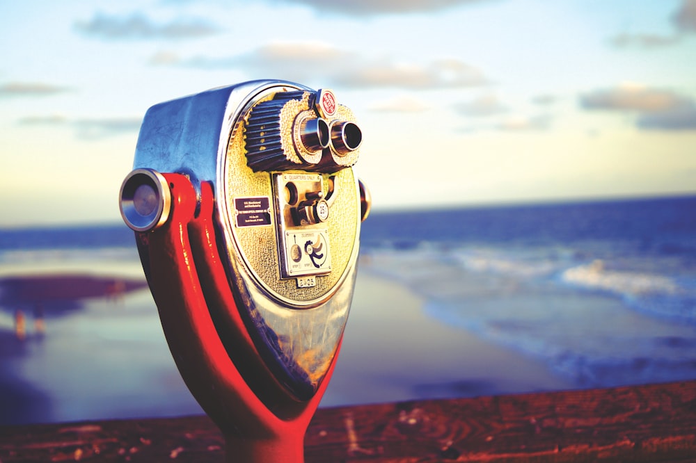 person holding red and silver coin operated telescope