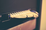 A network switch with multiple Ethernet cables plugged into its ports, positioned horizontally and bundled together with cable ties. The switch casing has visible brand markings and numeric labels near the ports.