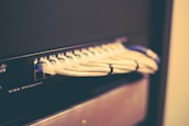 A network switch with multiple Ethernet cables plugged into its ports, positioned horizontally and bundled together with cable ties. The switch casing has visible brand markings and numeric labels near the ports.