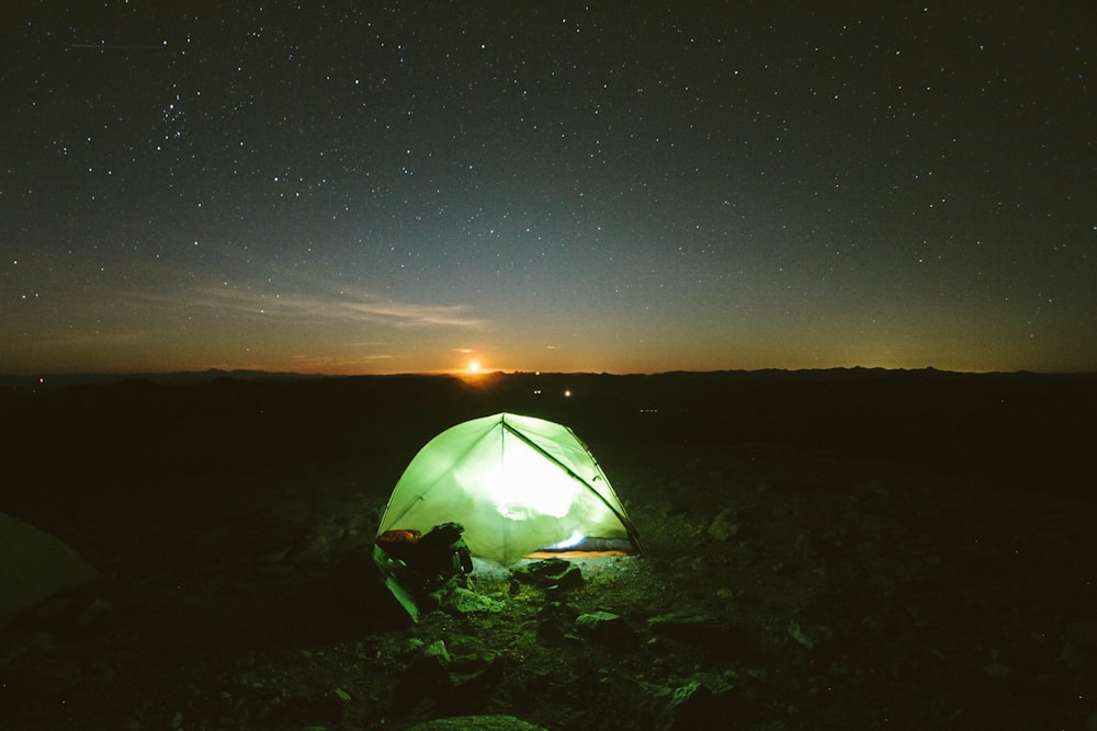 green camping tent with light inside at the field during sunset