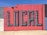 A vibrant mural painted on a concrete wall features the word 'LOCAL' in large, 3D-style letters. The wall is segmented into colorful blocks, primarily utilizing shades of red and blue, with a few sections in gray and white.