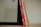 A set of six children's books with brightly colored spines, mostly red and yellow, leaning against the side of a black-framed mirror on a wooden surface.