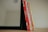 A set of six children's books with brightly colored spines, mostly red and yellow, leaning against the side of a black-framed mirror on a wooden surface.