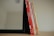 A set of six children's books with brightly colored spines, mostly red and yellow, leaning against the side of a black-framed mirror on a wooden surface.