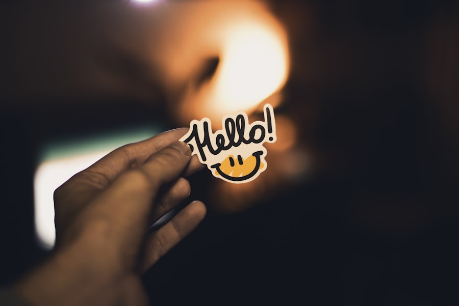 A hand holds up a sticker, which has a crudely-drawn smiley face and the word 'hello' on it.