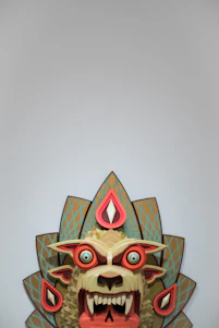Stylized lucha libre mask in teal, coral, yellow, and gold colors.