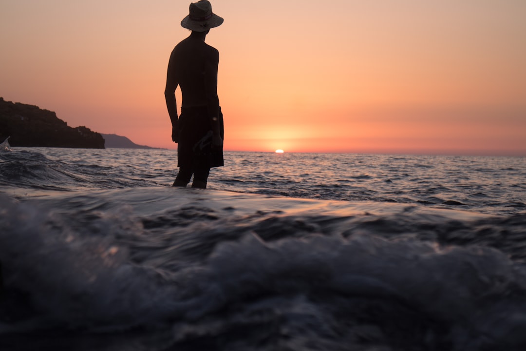 silhouette of person standing on shallow seashore facing sunset
