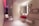 A modern bathroom with a sleek and minimalist design. It features a bold red sink mounted onto the wall below a large mirror that has a backlight. The wall next to the sink is decorated with various rectangular metal frame pieces of different sizes. There is a shelf below the sink holding rolled white towels. The room has a subtle and elegant lighting with a notable red accent light on the ceiling extending through the hallway. The floor is covered in light-colored tiles and the overall space has a contemporary and artistic feel with smooth surfaces and clean lines.