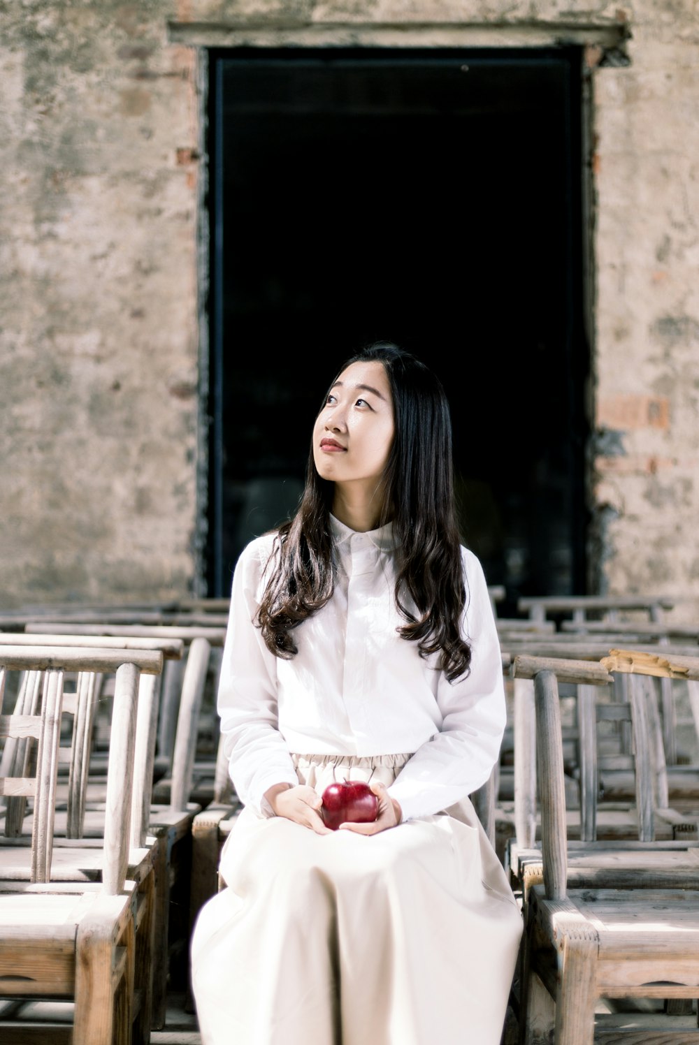 woman in white button-up dress shirt and white pants holding apple sitting on chair