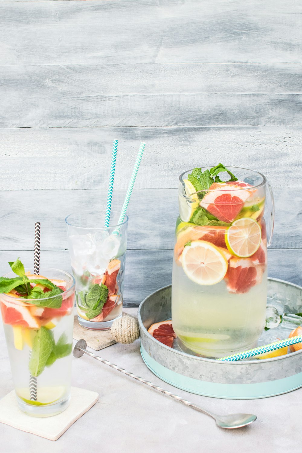 A cocktail table with a pitcher and two glasses filled with ice, lemons, grapefruits, mint, and more