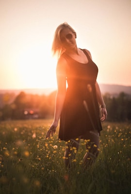 A model wearing layered necklaces and feather earrings, standing in a wildflower field at golden hour.