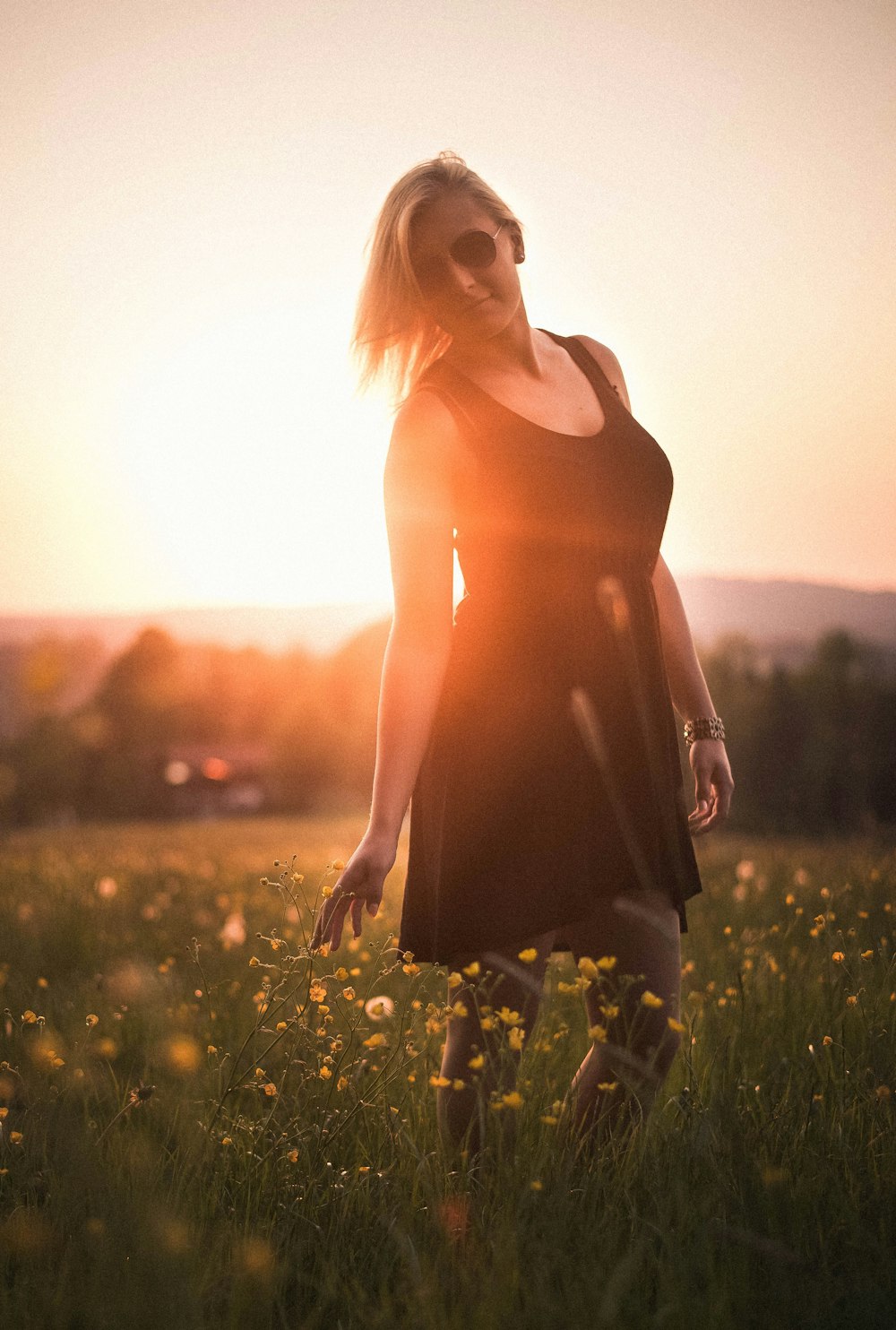 Frau trägt schwarzes Minikleid mit Rundhalsausschnitt, umgeben von Blumen während des Sonnenuntergangs