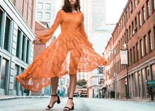 woman in orange long-sleeved dress between buildings during daytime