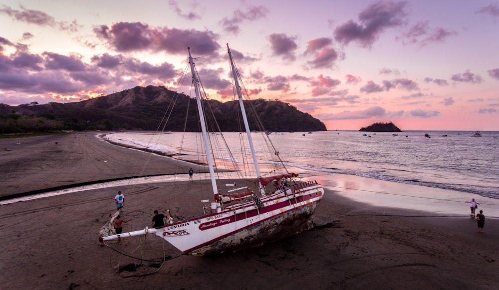 white and red sail boat on seashore