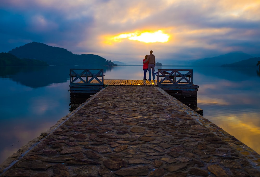 casal em pé no cais olhando para o pôr do sol