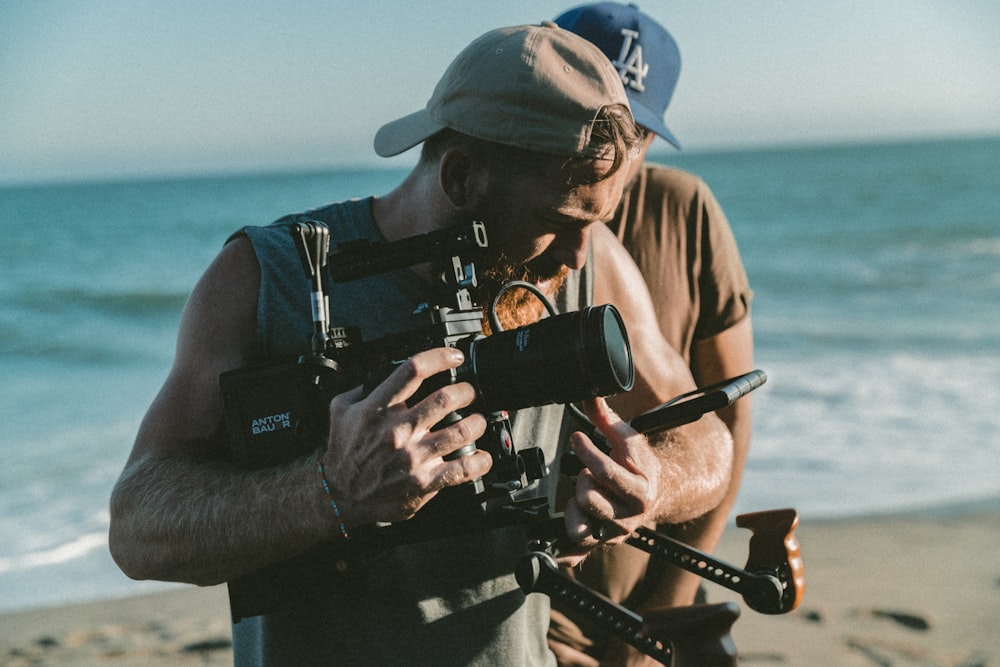 man holding video camera standing near body of water