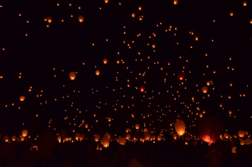 Numerous glowing lanterns float into a dark night sky, creating a mesmerizing display of warm lights scattered throughout the scene. The contrast between the black sky and the orange glow of the lanterns gives a sense of tranquility and celebration.