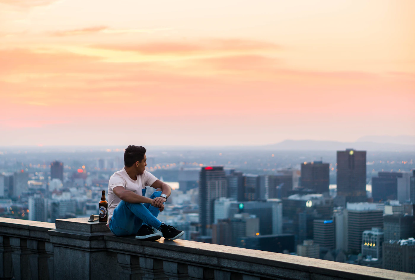 A person seated quietly beside tall city buildings, the outline of a life that looks secure from a distance