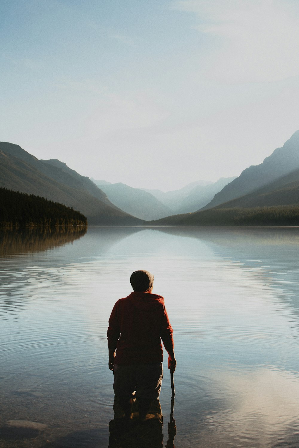 person standing on the lake in the middle of mountains