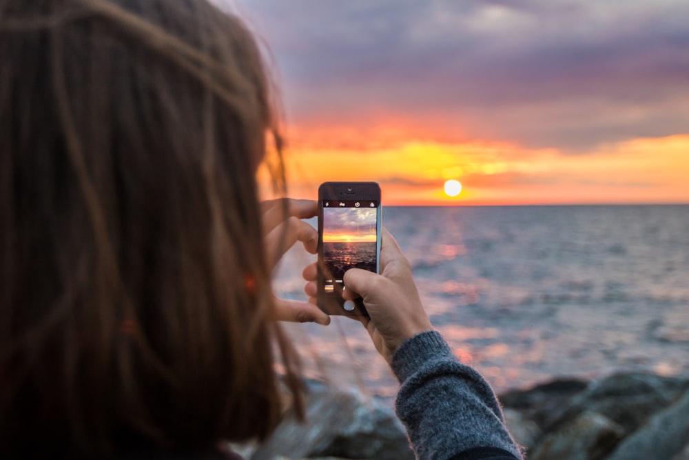 Frau mit Handy macht ein Foto vom Sonnenuntergang