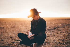 A scenic desert sunset with a silhouette of a person reading a novel outdoors