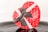 A heart-shaped gift box is prominently displayed, featuring a vibrant red color with small white heart patterns. The box is adorned with a brown ribbon with white polka dots, tied into a decorative bow. The words 'Love' and a message are printed in white on the box. The surface on which the box rests has a reflective quality, casting a slight reflection.