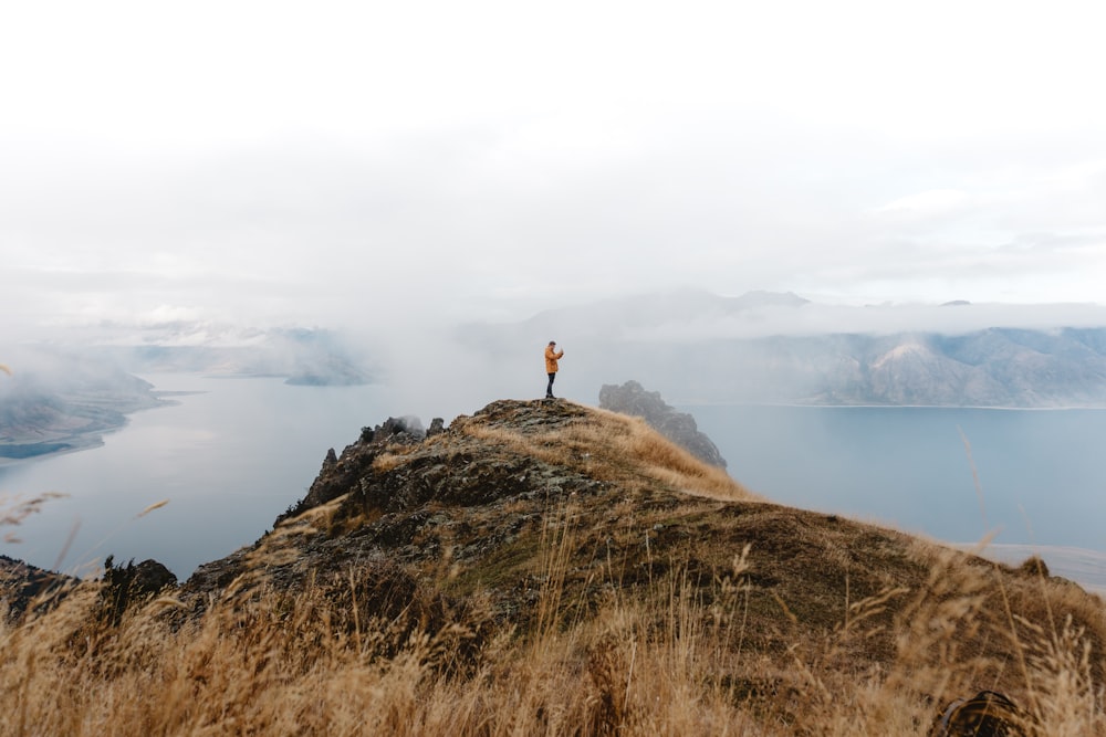 pessoa em pé no topo da colina perto do lago durante o dia