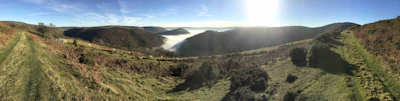 Panoramic view of a winding trekking trail disappearing into misty hills.