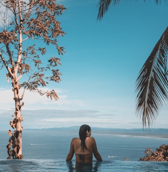 woman wearing black bikini tap swimming on body of water between trees