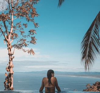 woman wearing black bikini tap swimming on body of water between trees