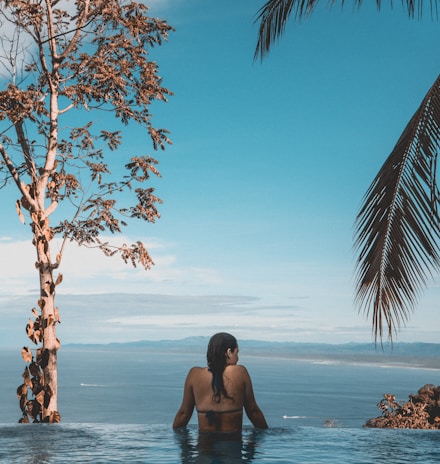 woman wearing black bikini tap swimming on body of water between trees