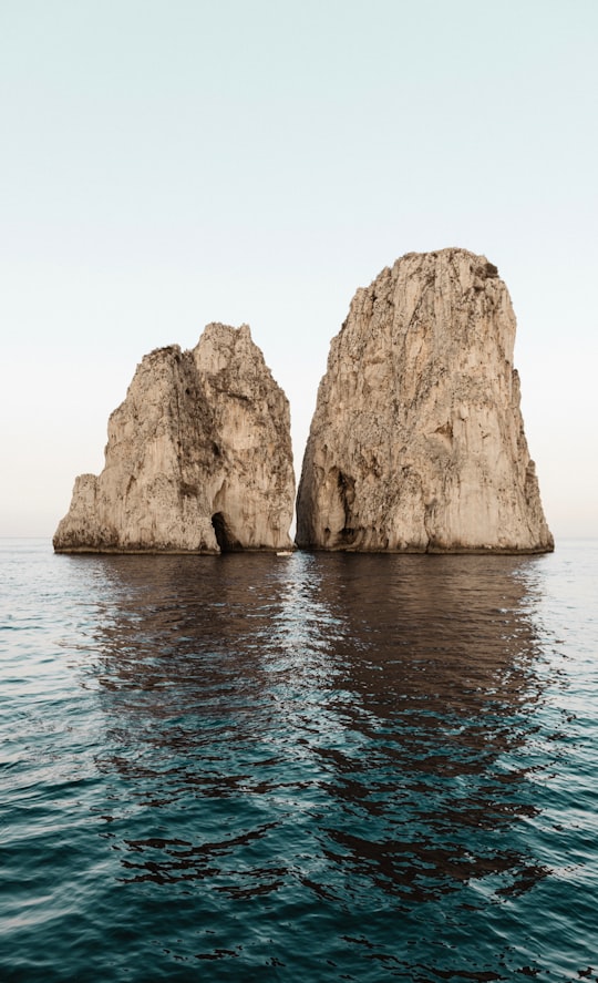 two beige rock formations on body of water in Faraglioni Italy
