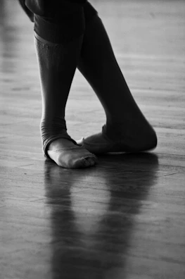 A close-up of a dancer’s feet mid-step on a polished wooden floor.