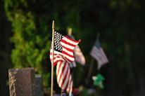 An American flag gently waving beside a field of white crosses marking graves of fallen soldiers.